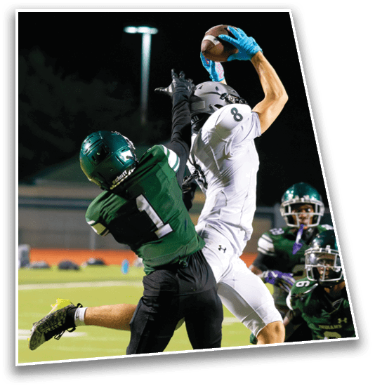 Two people in football uniforms are reaching for a football during a nighttime game. Description generated by AI