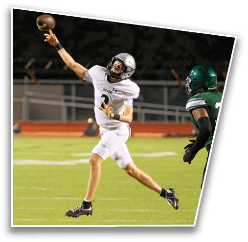 An adult in a white football uniform is throwing a football while another adult in a green football uniform with the number 33 is approaching on a grassy field. Description generated by AI