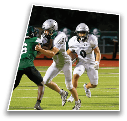 Two people in white football uniforms are running on a field while one person in a green uniform attempts to block them during a game. Description generated by AI