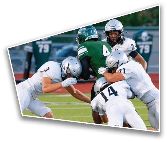 Four people in football uniforms are engaged in a tackle on a green field during a game. Description generated by AI