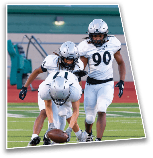 A person wearing a silver football helmet and a white jersey with the word Guyer and the number 90 is on a football field. Description generated by AI