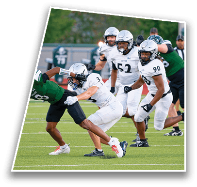 People in white and green football uniforms are actively engaged in a tackle on a grassy field during a game. Description generated by AI