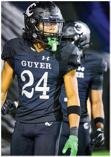 A person wearing a black football uniform with the number 24 and the word Guyer on the front is standing on a field with another player blurred in the background. Description generated by AI