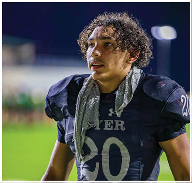 A person wearing a dark football jersey with the number 20 and a towel draped around their neck stands on a field. Description generated by AI