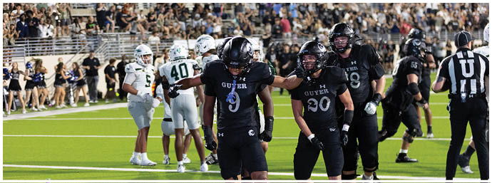 Adults in black football uniforms celebrate on a green field while adults in white uniforms and cheerleaders stand in the background. Description generated by AI
