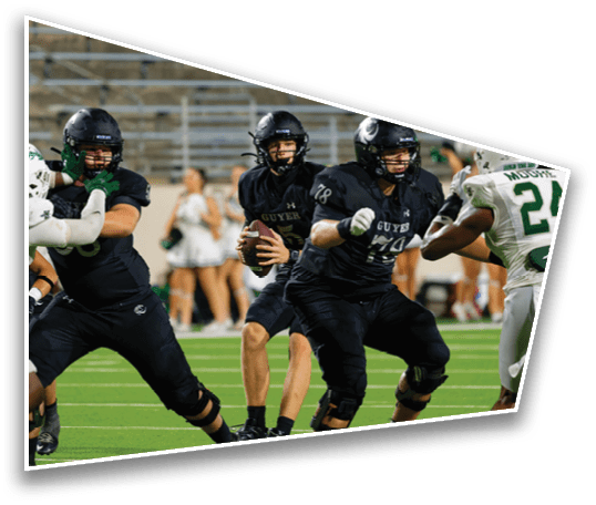 People in football uniforms are engaged in a play on a field with one person holding the ball and others blocking or attempting to tackle. Description generated by AI