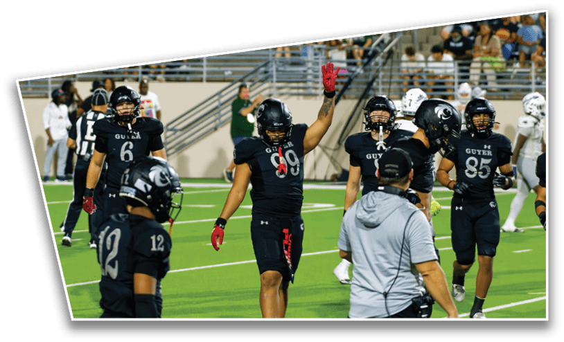Several people in black football uniforms are on a green field, with one raising a hand and others standing or walking nearby. Description generated by AI