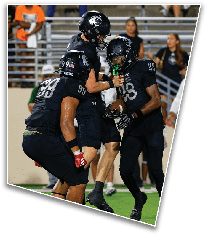 Two people wearing black football helmets and uniforms are engaged in a game with spectators sitting on bleachers in the background. Description generated by AI