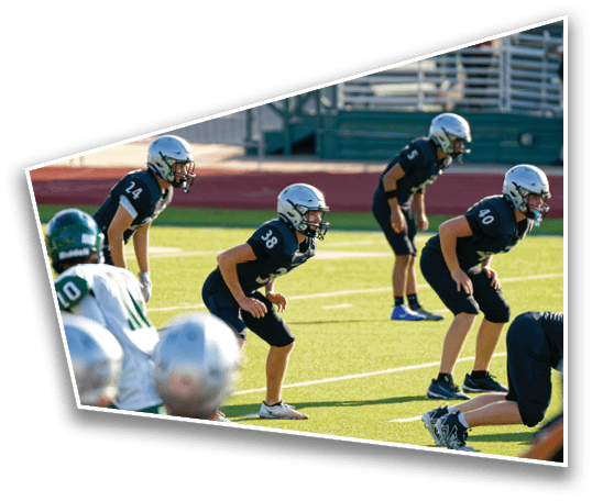 Several people in football uniforms and helmets are positioned on a field, appearing ready for a play during a game. Description generated by AI