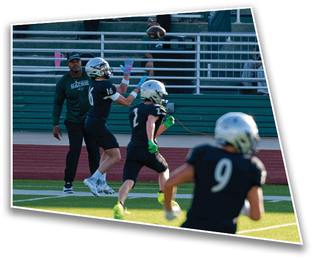 People in football uniforms are on a field with one person preparing to catch a football while others watch or move nearby. Description generated by AI