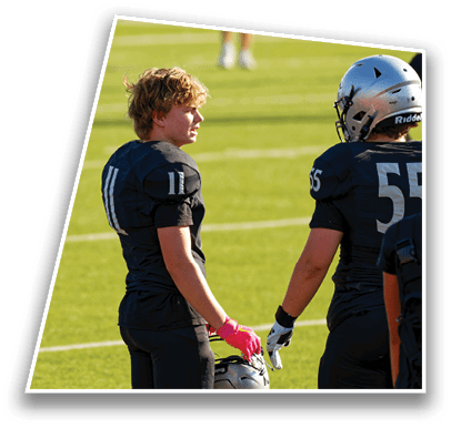 A person in a white football uniform is preparing to throw a football on a green field while another person in a similar uniform is positioned nearby. Description generated by AI