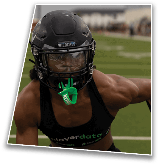 A person wearing a black football helmet with a green mouthguard is on a football field with blurred spectators in the background. Description generated by AI