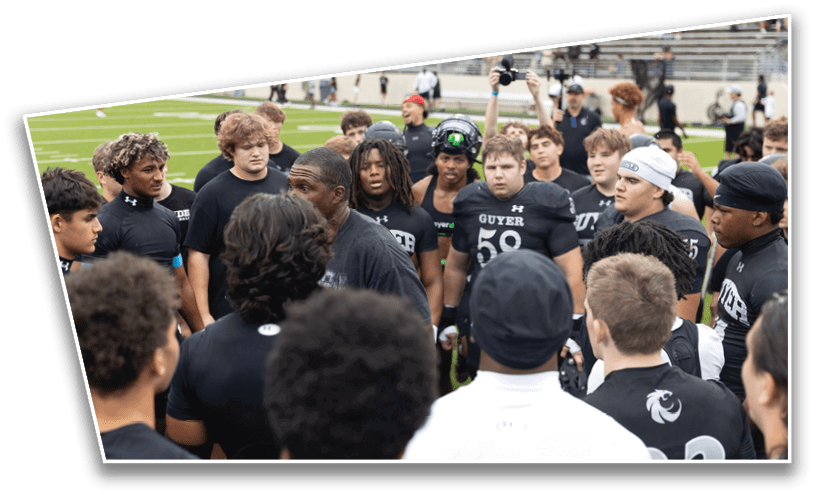 A group of people wearing black athletic shirts are gathered closely on a sports field, appearing to listen attentively to a person speaking in the center. Description generated by AI