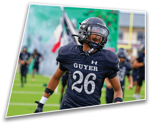 A person wearing a dark football uniform with the number 26 and the word Guyer is running on a green field with other players in the background. Description generated by AI