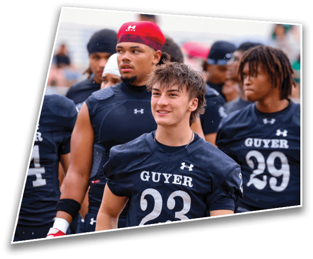 A group of people wearing black football uniforms with “GUYER" and numbers on them are standing together, with one person in the foreground smiling. Description generated by AI