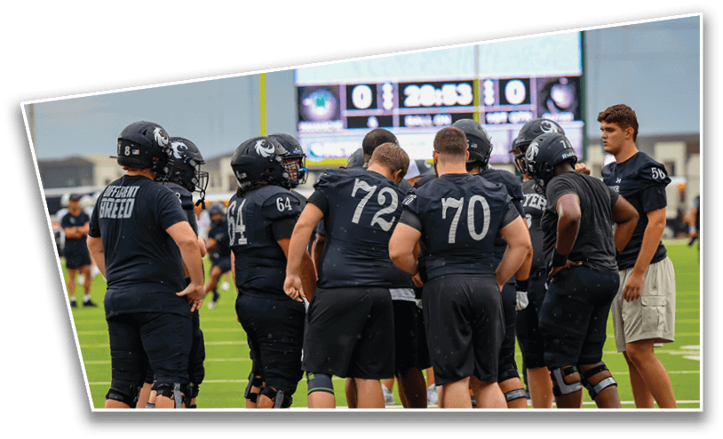 Four people wearing white football uniforms with the word “GUYER" stand side by side on a field with a blurred crowd in the background. Description generated by AI