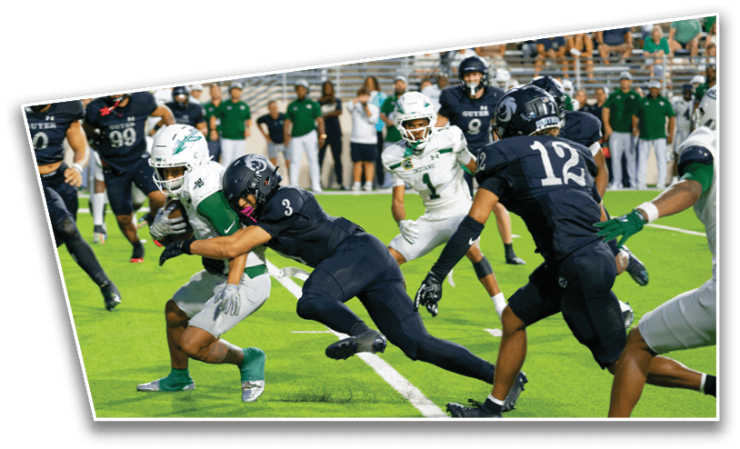 A group of people in football uniforms are actively engaged in a tackle on a green field with spectators in the background. Description generated by AI