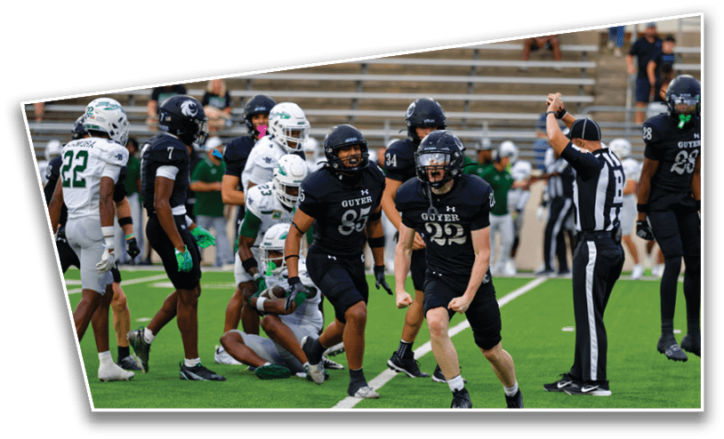 Players in black and white football uniforms are on a green field with one player in black celebrating while a referee signals a call. Description generated by AI