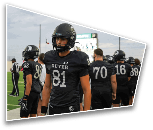 People wearing black football uniforms with helmets stand on a green field, with one person in the foreground wearing number 81 and the word “GUYER" on the jersey. Description generated by AI
