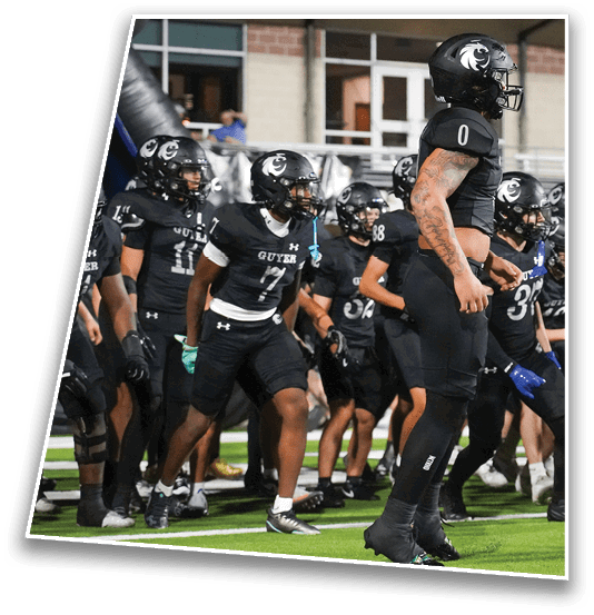 A group of people wearing black football uniforms and helmets are gathered on a field, appearing to prepare for a play or drill. Description generated by AI