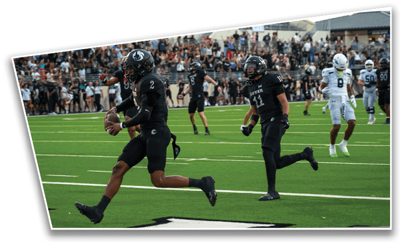 People in football uniforms are playing on a field with a crowd watching from the stands in the background. Description generated by AI