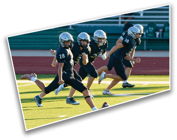 A group of people wearing helmets and sports uniforms are running on a football field with one person kicking a football. Description generated by AI