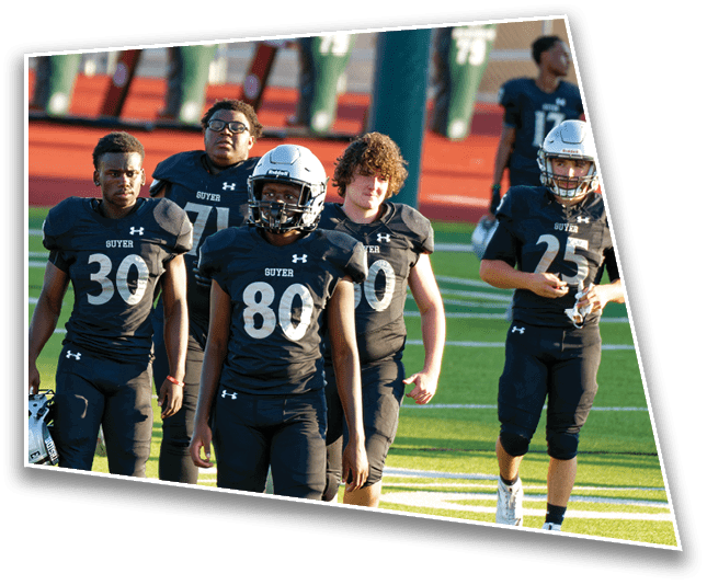 Five people wearing black football uniforms with white helmets are walking on a football field during daylight. Description generated by AI