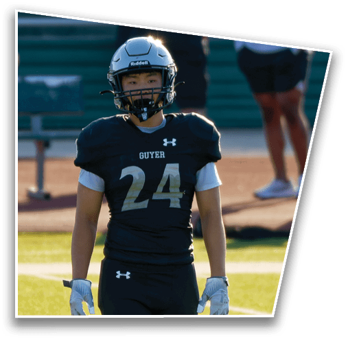 A person wearing a black football uniform with the number 24 and a helmet stands on a field. Description generated by AI