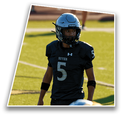 A person wearing a black football uniform with the number 5 and a helmet stands on a grassy field looking to the side. Description generated by AI