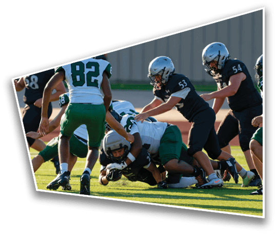 People in sports uniforms are engaged in a football tackle on a grassy field during a game. Description generated by AI