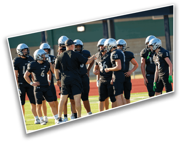 A group of people wearing football helmets and black uniforms are gathered on a field while one person in black sportswear appears to be giving instructions. Description generated by AI