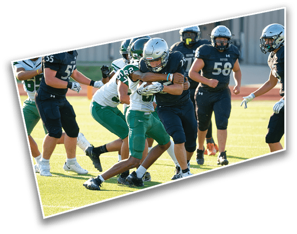 Players in football uniforms are actively engaged in a tackle during a game on a sunlit field. Description generated by AI