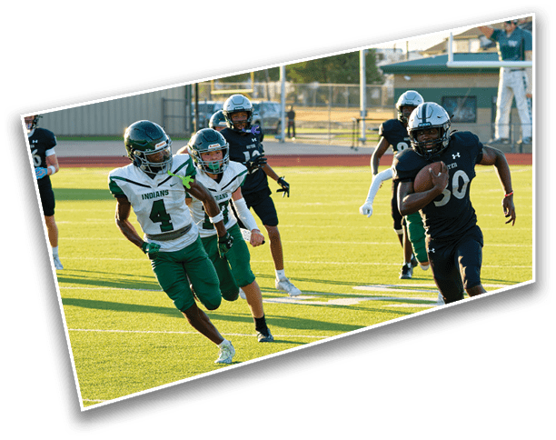 People in football uniforms are actively running on a sunlit field with one person holding a football while others chase. Description generated by AI