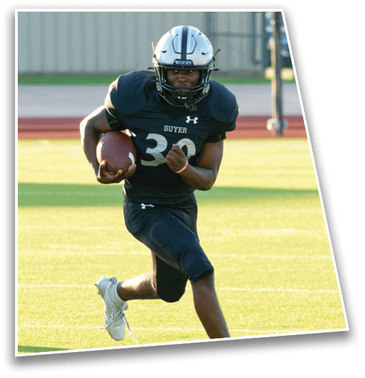 A person wearing a football uniform and helmet is running on a field while holding a football. Description generated by AI
