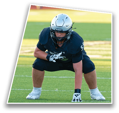 A person wearing a football helmet and uniform is crouched in a ready stance on a grassy field. Description generated by AI