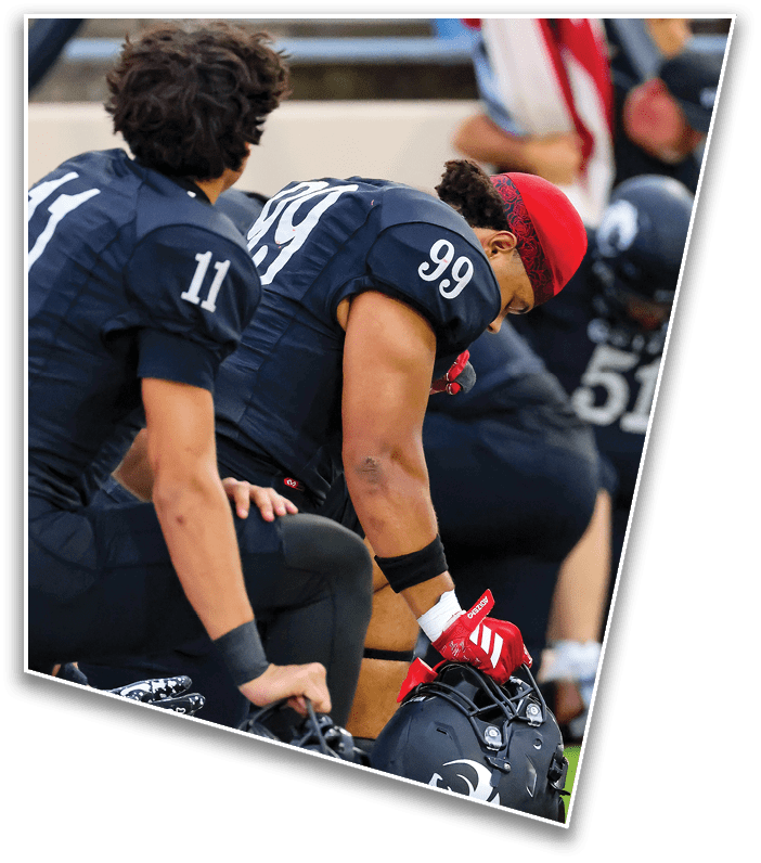 Two people wearing dark sports jerseys with numbers 99 and 11 are leaning forward, likely on a sports field or bench. Description generated by AI