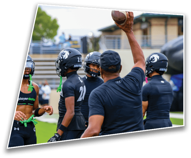 A group of people wearing black sports uniforms and helmets are gathered on a field while one person raises a football in the air. Description generated by AI