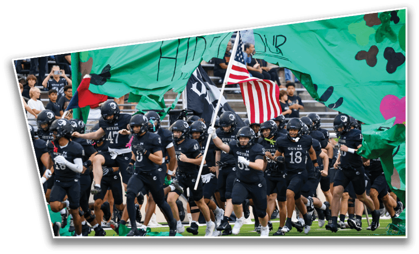A group of people in black sports uniforms run through a torn green banner while one person holds an American flag. Description generated by AI