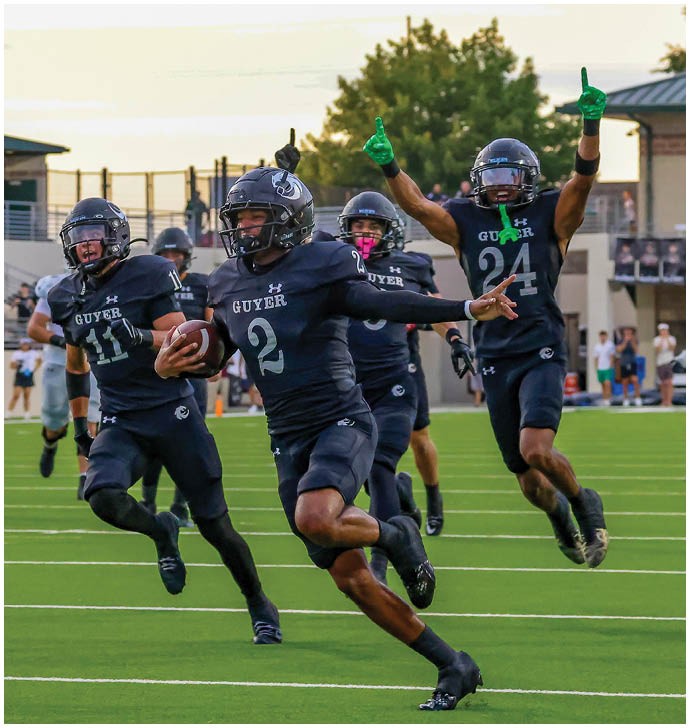 Several people wearing athletic clothing and cleats are running on a green sports field with white yard lines. Description generated by AI