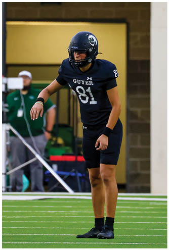 A person wearing a black football uniform with the number 81 and the word “GUYER" stands on a green field preparing for a play. Description generated by AI