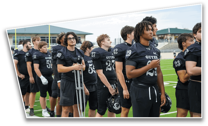 A group of people wearing black sports uniforms stand in a line on a football field, with one person holding crutches. Description generated by AI