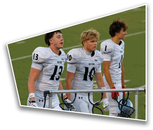 Three people wearing white football uniforms with numbers 13, 10, and 1 stand on a green field, appearing focused and attentive. Description generated by AI