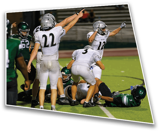 People in football uniforms are on a field with some standing and raising their arms while others are on the ground during a game. Description generated by AI