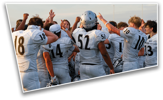 A group of people wearing white football uniforms with numbers are gathered closely together, raising their fists and hands in a celebratory or motivational gesture outdoors. Description generated by AI