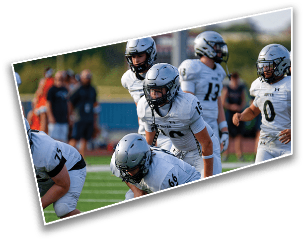 A group of football players in white uniforms and helmets are positioned on a field preparing for a play during a game. Description generated by AI