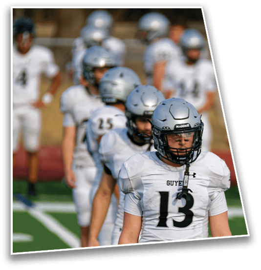 A group of people wearing silver helmets and white football uniforms stand in a line on a sports field. Description generated by AI