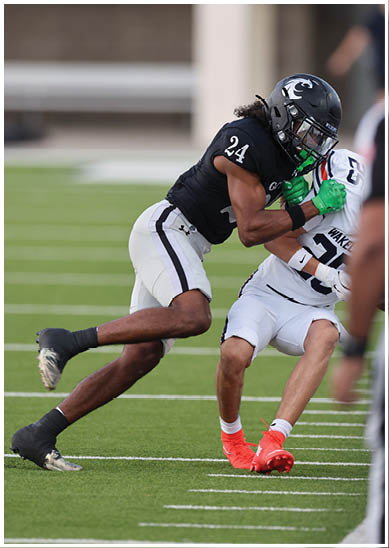 Two people wearing football uniforms are engaged in a tackle on a grassy field during a game. Description generated by AI