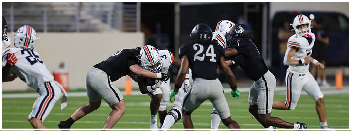 People in football uniforms are actively engaged in a play on a football field with some players tackling and others running. Description generated by AI