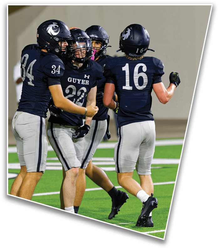 Four people wearing black football uniforms and helmets are celebrating on a green football field. Description generated by AI