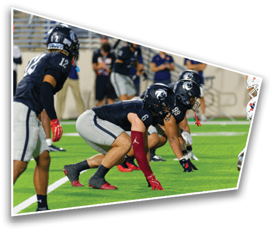 Two opposing American football teams are lined up facing each other on a green field, preparing for a play. Description generated by AI